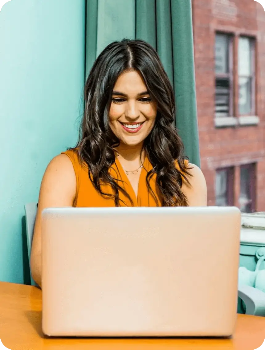 A woman smiles while working on a laptop, showcasing a positive and engaged expression.