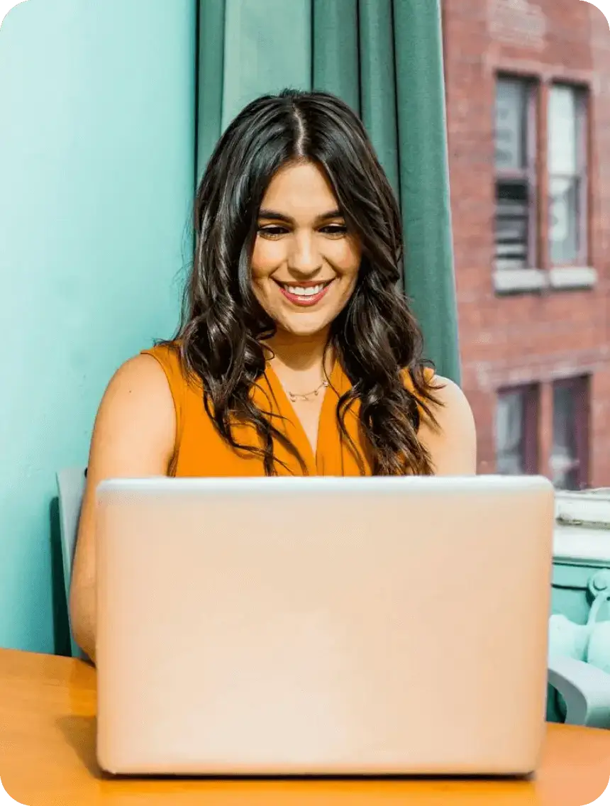 A woman smiles while working on a laptop, showcasing a positive and engaged expression.