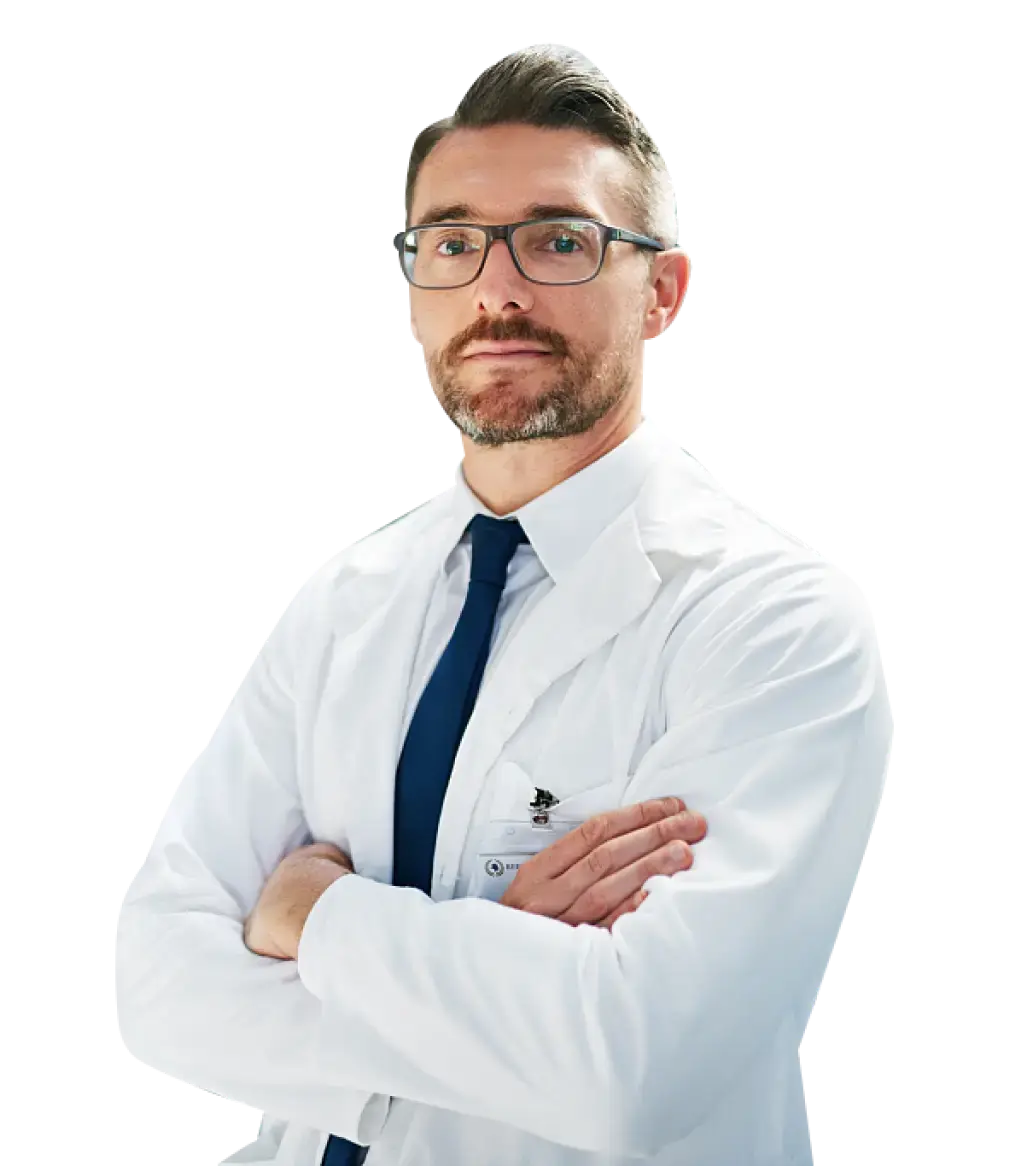 A male provider wearing a lab coat and tie, standing confidently in a clinical setting.