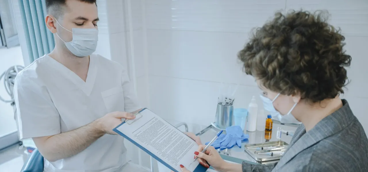 A man and woman converse over a document in a dental office, surrounded by dental equipment and a welcoming atmosphere.