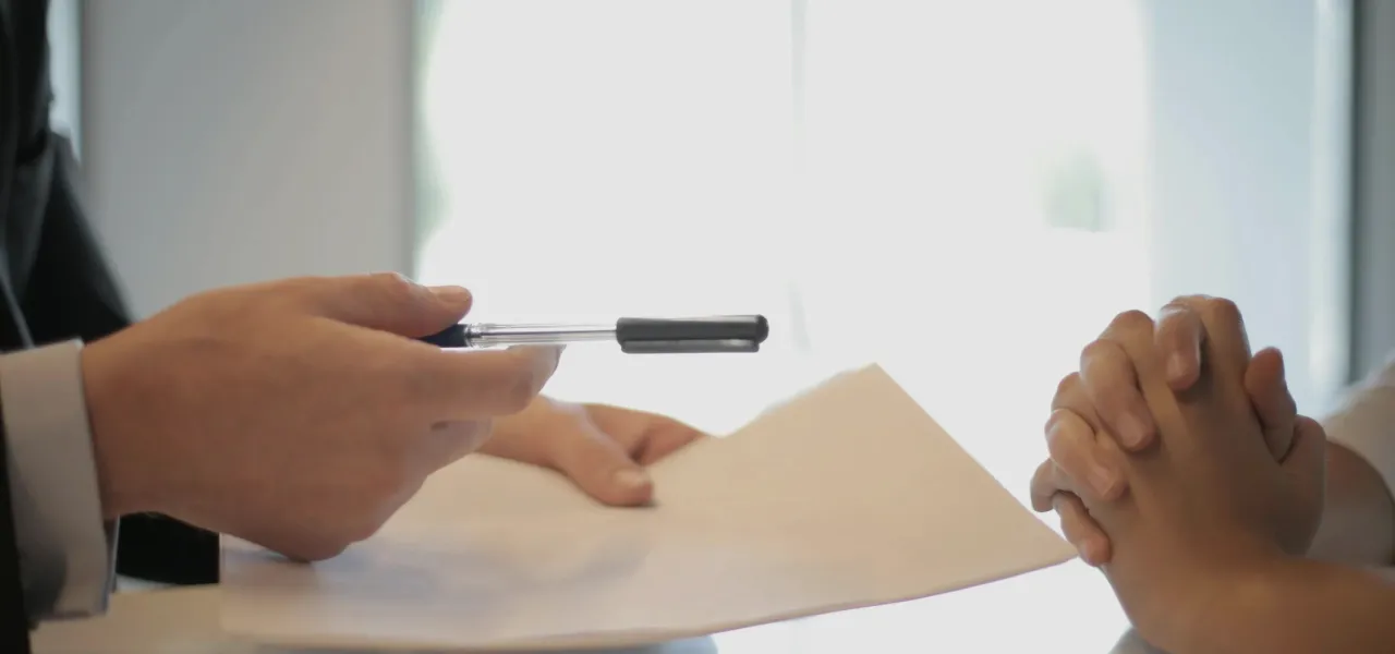 A man and woman sit at a table, engaged in writing with a pen and paper, focused on their task.