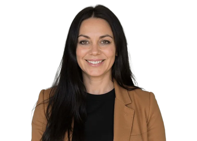 A woman with long black hair wearing a brown jacket stands confidently, showcasing her style and poise.