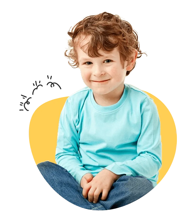 A young boy sits on the floor, hands in pockets, looking relaxed and contemplative.